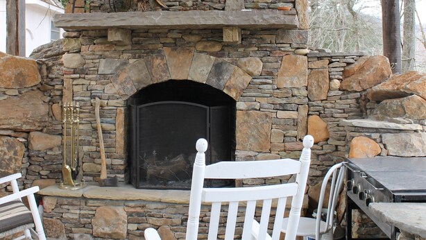 A stone fireplace with a black hearth, surrounded by white chairs and a table. - Big Nate Cabin on Lake with Water Trampoline (Hiawassee)