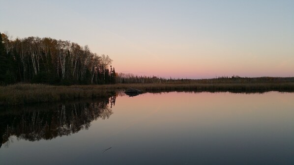 A calm lake reflecting trees and a clear sky.
