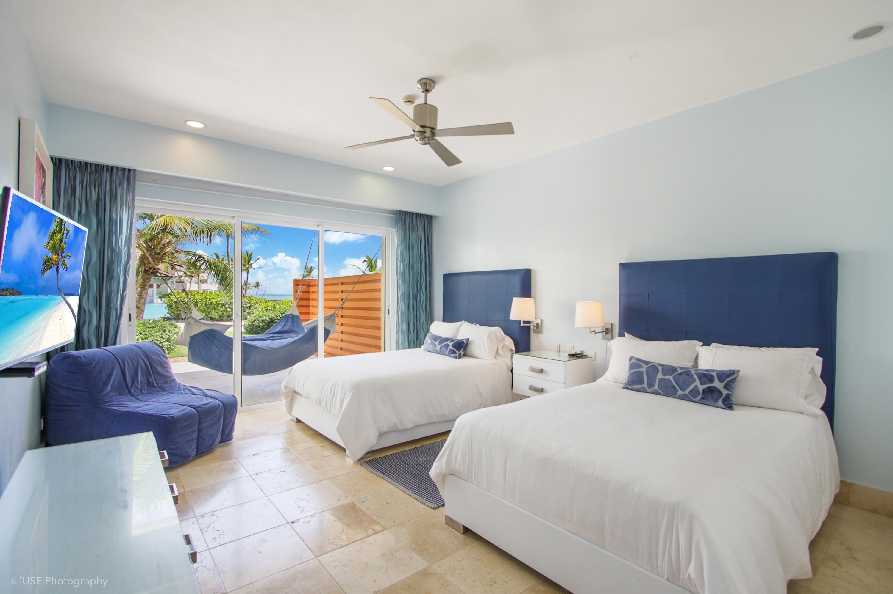 A hotel room with two beds, a ceiling fan, a TV, and a view of the outdoors.