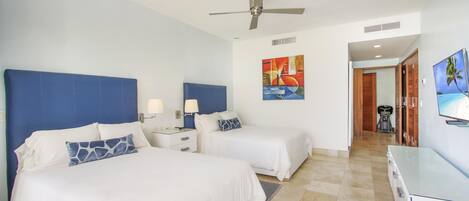 A hotel room with two beds, a ceiling fan, artwork on the walls, and a TV on the wall.
