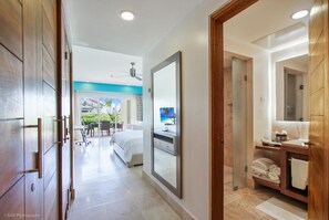 A modern hotel room with a large bed, a bathroom with a mirror and sink, and a view of the outside balcony.