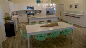 A modern kitchen with white cabinets, a central island with stools, and a dining table with chairs. - Beachfront! 4bdr(3 kings)/3 bath/sleeps  17  (Surfside Beach)