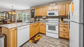 Una cocina moderna con armarios de madera, un lavavajillas blanco, un horno empotrado y un refrigerador de acero inoxidable.