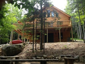 A wooden cabin with a balcony, surrounded by trees and rocks. - Log Home Nestled Between The White Mountains and The Lakes Region (Campton)