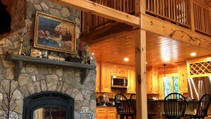 A rustic cabin interior with a stone fireplace, wooden dining area, and a kitchen with wooden cabinets.