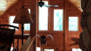 A cabin interior with a high ceiling, wooden walls, a staircase, and a view of the outside.