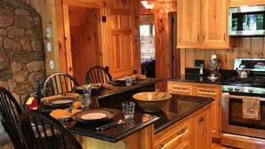 A wooden cabin interior with a dining area, kitchen, and stone wall.
