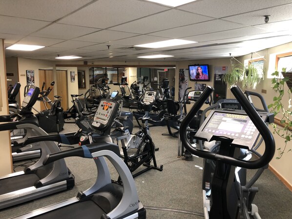 A gym with multiple cardio machines, a television screen, and a motivational poster.