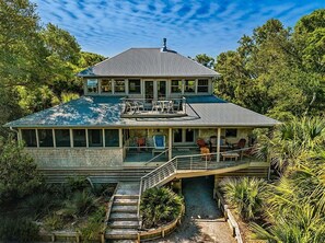 A two-story house with a covered porch, a staircase, and a view of the surrounding greenery.