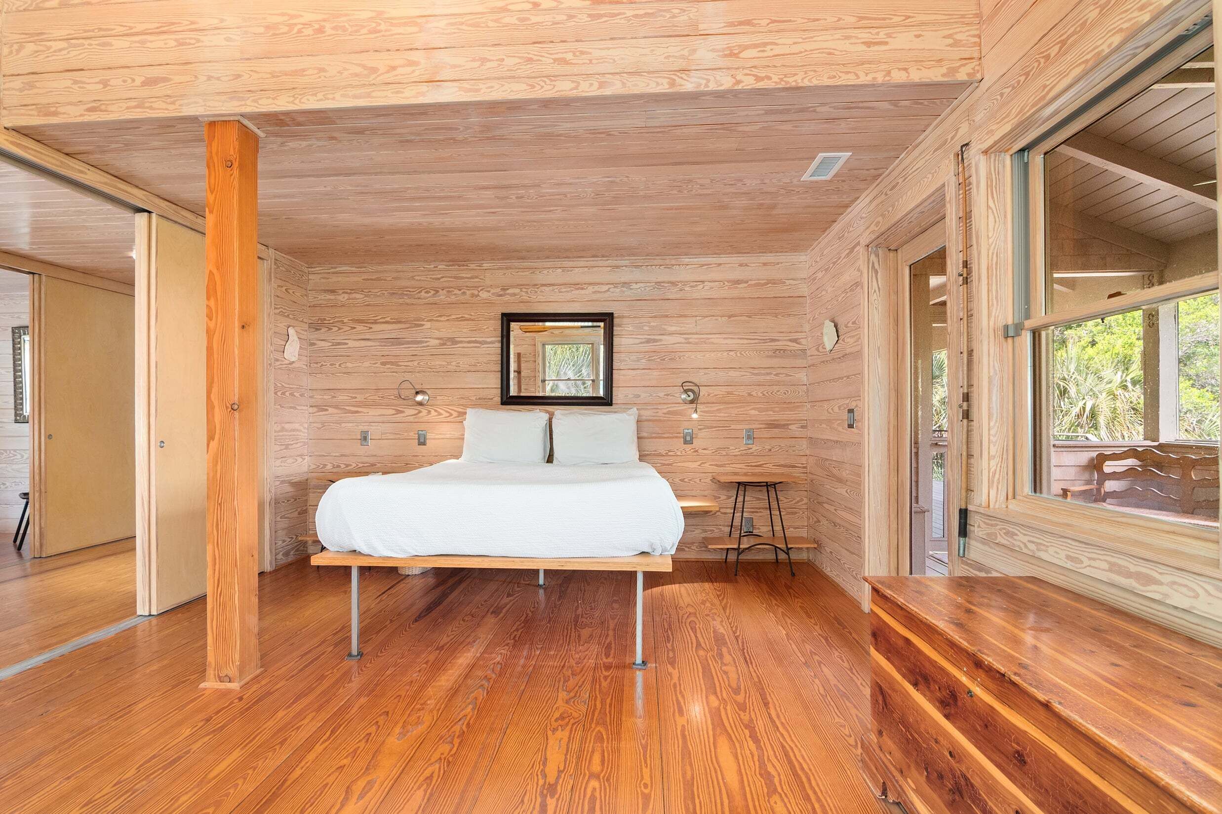 A wooden-paneled bedroom with a bed, bedside lamps, and a window.