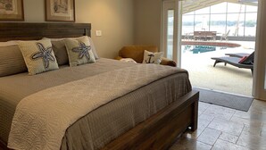 A bedroom with a large bed, two framed pictures on the wall, and a view of a pool area through a glass door.