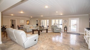 A spacious living room with a large white sofa, a coffee table, and a grey armchair. There are multiple doors leading to other rooms, and a television is mounted on the wall.