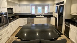 A modern kitchen with white cabinetry, a black countertop, and a central island with two chairs.