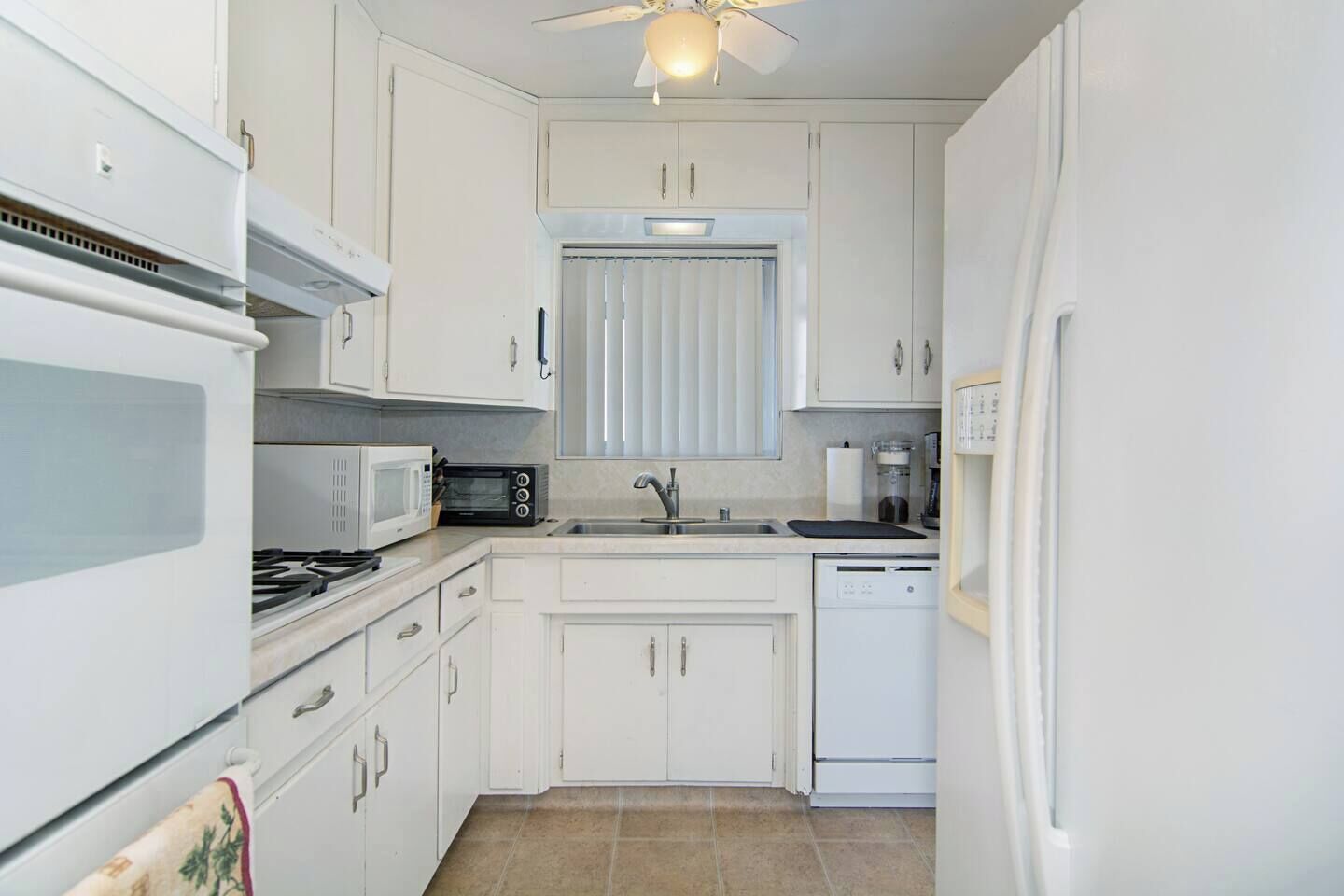 A compact kitchen with white cabinets, a microwave, a stove, a sink, and a dishwasher.