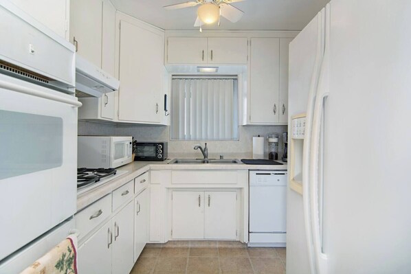 A compact kitchen with white cabinets, a microwave, a stove, a sink, and a dishwasher.