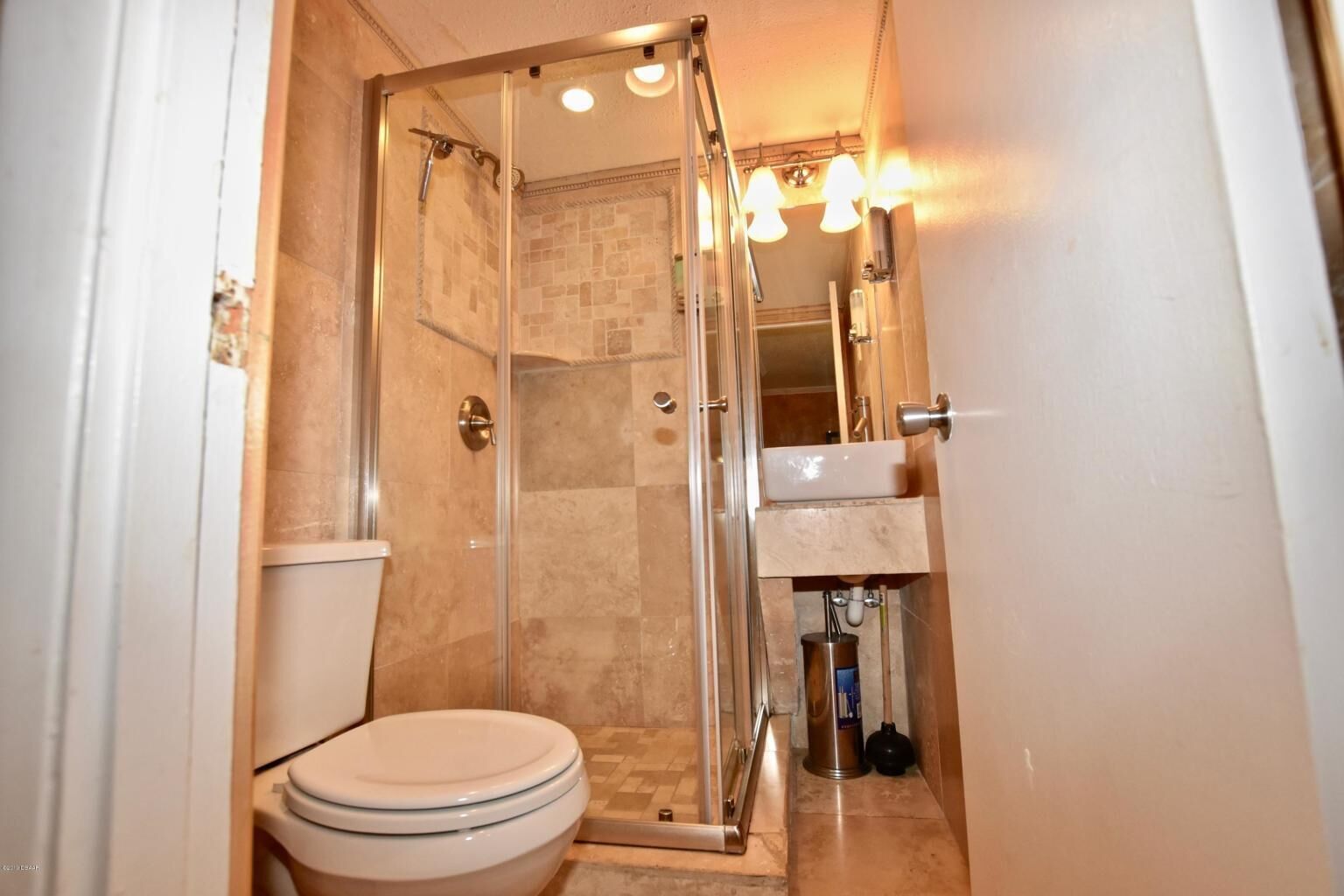 A compact bathroom with a glass-enclosed shower, a toilet, and a sink with a mirror above it.