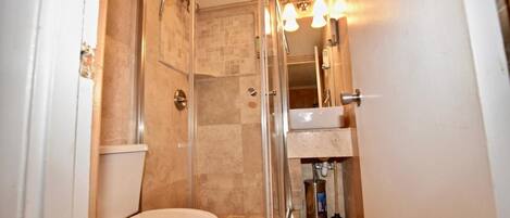 A compact bathroom with a glass-enclosed shower, a toilet, and a sink with a mirror above it.