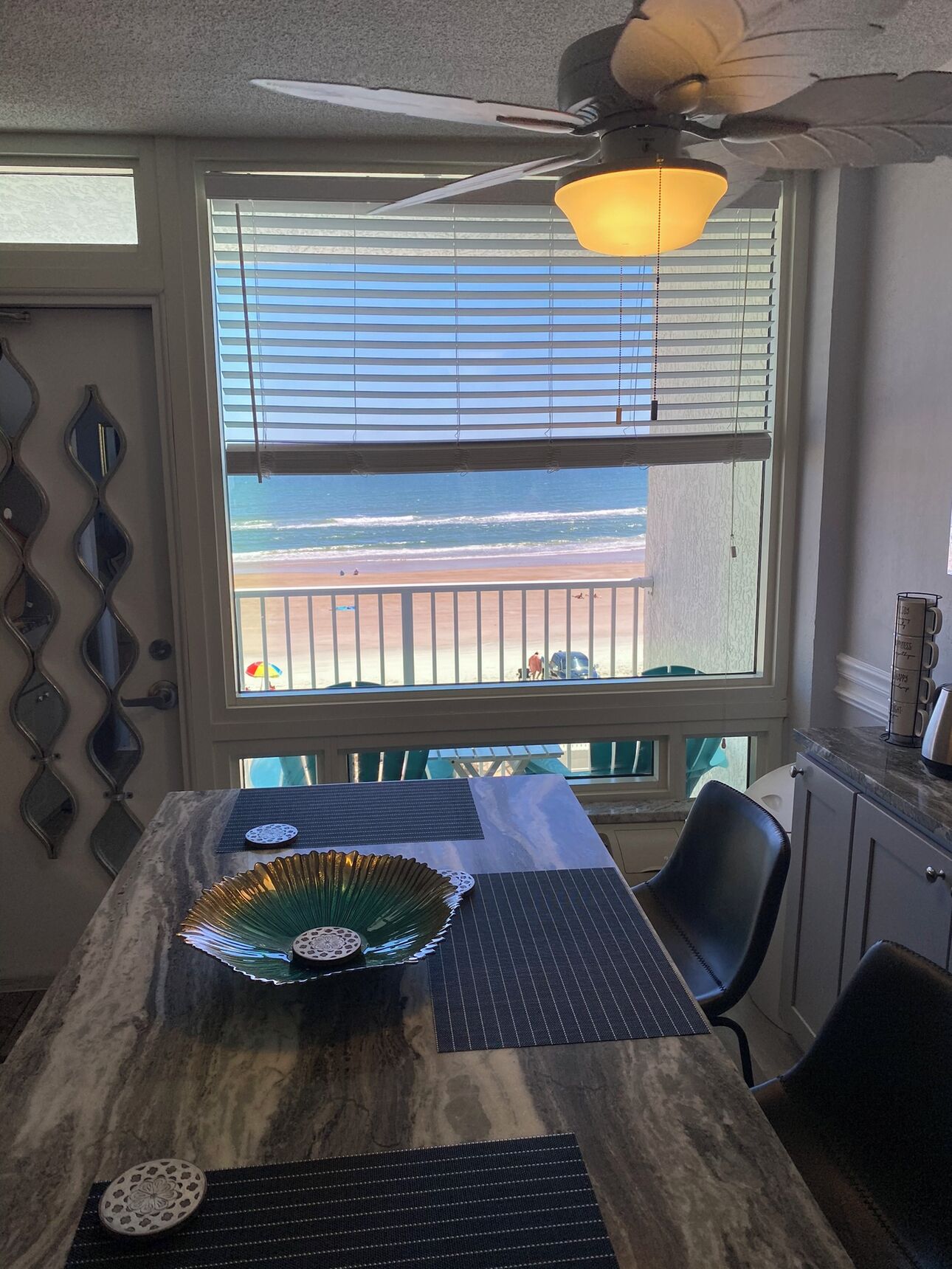 A dining area with a view of the beach, a ceiling fan, and a table with decorative items.