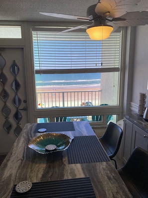 A dining area with a view of the beach, a ceiling fan, and a table with decorative items.