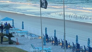 Eine Terrasse direkt am Strand mit Außenbestuhlung, einer Fahnenstange mit Wimpel und Blick auf den Ozean.