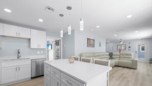 A modern kitchen with white cabinetry, a central island, and pendant lighting. - Zénith Retreat steps from the sugary sand (Fort Myers Beach)