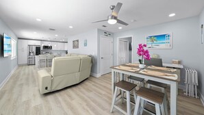 A modern living space with a sofa, dining table, and chairs, a ceiling fan, recessed lighting, and a kitchen area in the background. - Zénith Retreat steps from the sugary sand (Fort Myers Beach)