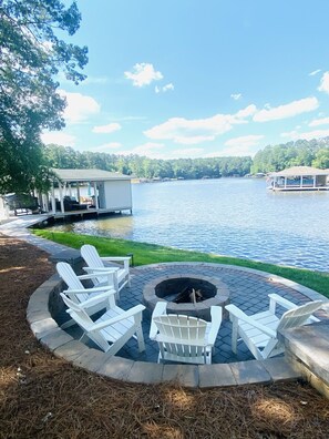 A lakeside deck with Adirondack chairs, a fire pit, and a view of the lake and docked boats.