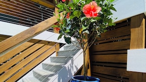 Una terraza de madera con una maceta azul y flores rojas.