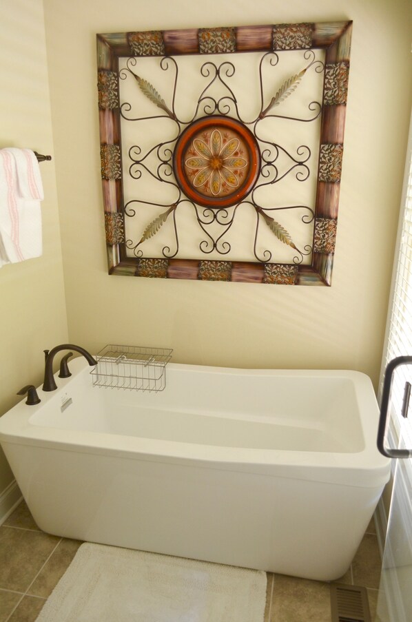 A bathroom with a freestanding bathtub, a towel rack, and a decorative wall piece above the tub.
