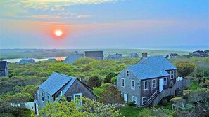 Stunning coastal home with a traditional pitched roof and inviting front porch, nestled among other residences near the ocean.