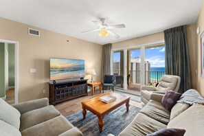 A living room with a television, a coffee table, a sofa, a chair, and a balcony with a view of the ocean. - Ariel Dunes I 1409*Extra bunk room and 3 pools! (Miramar Beach)