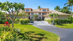 A multi-story residential building with a driveway leading to the entrance, surrounded by well-maintained lawns and tropical plants. - Hilton Pool Pass  for stays in 2026. Waikoloa Beach Villas C23 (Waikoloa Beach Resort)
