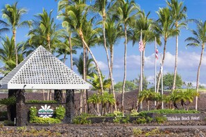 A sign for Waikoloa Beach Resort with a triangular structure and palm trees in the background.
