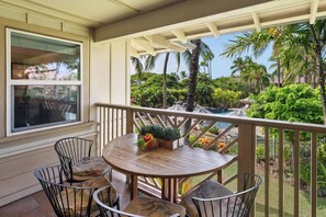 A wooden deck with a table and chairs, overlooking a pool and lush greenery. - Hilton Pool Pass  for stays in 2026. Waikoloa Beach Villas C23 (Waikoloa Beach Resort)