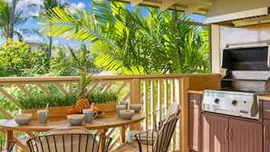 An outdoor kitchen area with a grill, a dining table with chairs, and a view of lush greenery. - Hilton Pool Pass  for stays in 2026. Waikoloa Beach Villas C23 (Waikoloa Beach Resort)