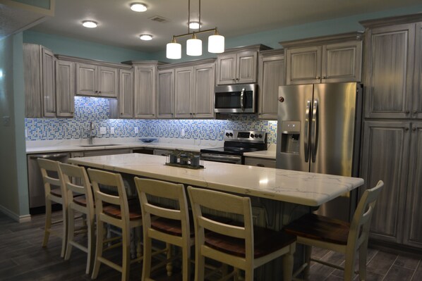 A modern kitchen with a central island, stainless steel appliances, and a tiled backsplash.