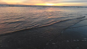 Une plage au coucher du soleil, où les vagues viennent doucement lécher le rivage.