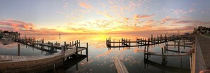 A waterfront pier with wooden walkways and docks extending into calm water, reflecting the sunset sky.