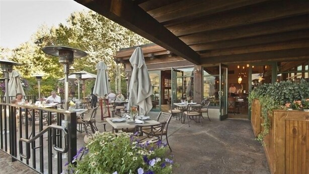 Een buitenterras met tafels en stoelen, omringd door potplanten en parasols.