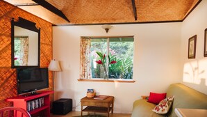 Una sala de estar con un televisor sobre un soporte rojo, una mesita con una cesta, un sofá con cojines rojos y una ventana con cortinas.