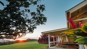 Una casa con porche cubierto, jardín y vista al atardecer.