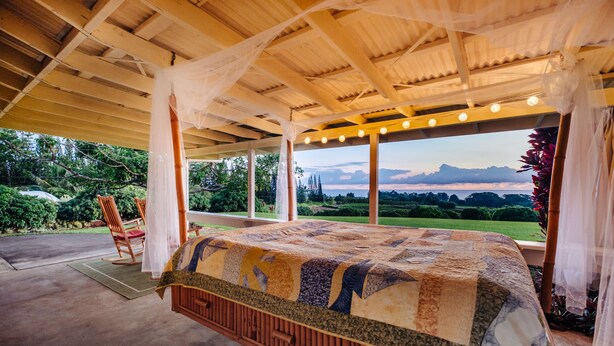 Una cama grande con colcha, techo de madera y vista a un paisaje.
