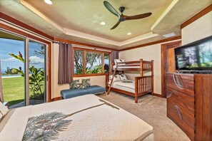 Una camera da letto con un letto a castello, una TV a schermo piatto, un letto con motivo tropicale e vista su un prato e degli alberi.