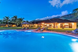 Un resort con piscina, lettini e un edificio ben illuminato dotato di area patio.