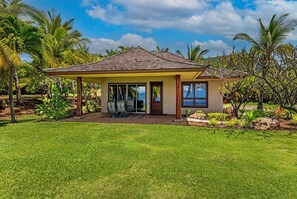Una casa con veranda coperta, prato e vegetazione tropicale.