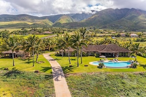 Resort com piscina, palmeiras e montanhas ao fundo.