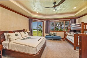 A bedroom with a bed, a bench, a desk, and a view of the outdoors.