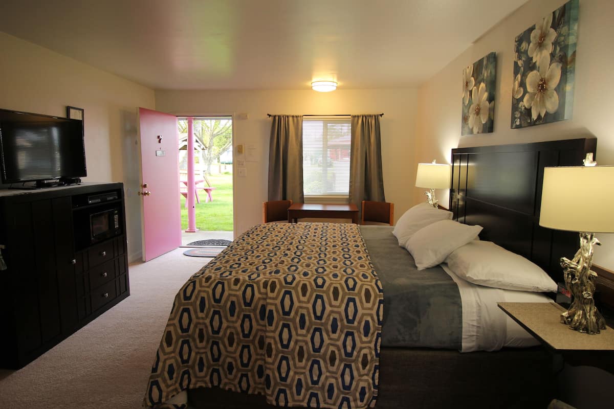 A hotel room with a bed, bedside lamps, a TV, a desk, and a window with curtains.