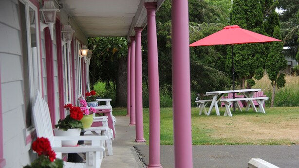 Une véranda avec des chaises blanches et roses, un parasol rouge et une table de pique-nique.