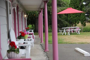A covered porch with white and pink chairs, a red umbrella, and a picnic table. - Mariner's Cove Inn (Westport)